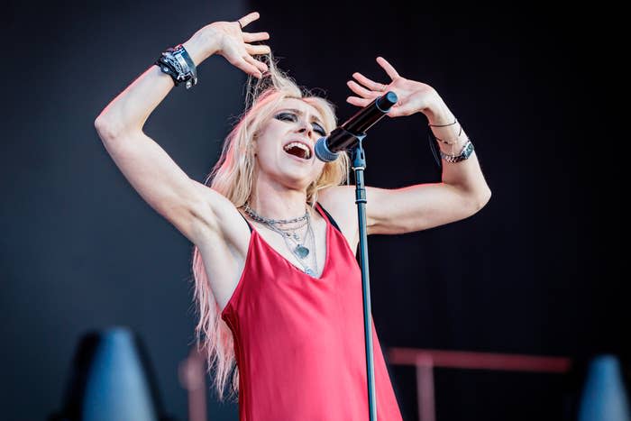 Taylor Momsen singing energetically on stage, wearing a sleeveless dress, multiple necklaces, and wristbands