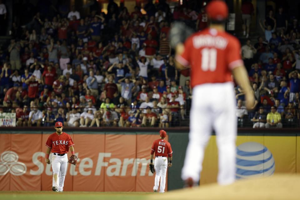 Texas Rangers starting pitcher Yu Darvish, watches from the mound as Rougned Odor, left rear, and right fielder Alex Rios, right rear, walk back to their positions after a ball fell between them allowing Boston Red Sox's David Ortiz to reach first in the seventh inning of a baseball game, Friday, May 9, 2014, in Arlington, Texas. An error was charged to Rios ending a try at a perfect game for Darvish in the 8-0 Rangers win. (AP Photo/Tony Gutierrez)