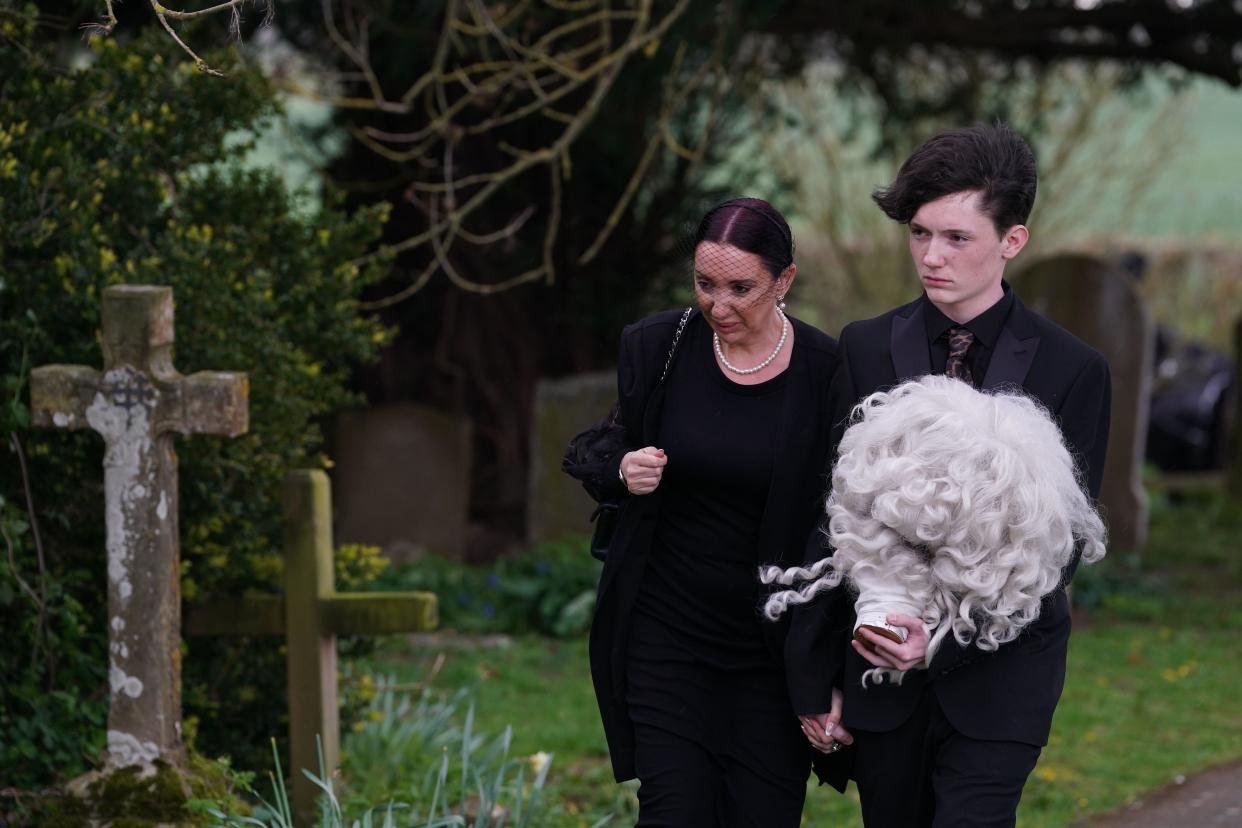 Daughter of Paul O'Grady, Sharyn Mousley, with an unidentified young man carrying holding the wig of Lily Savage arriving for the funeral of Paul O'Grady at St Rumwold's Church in Aldington, Kent. Picture date: Thursday April 20, 2023.