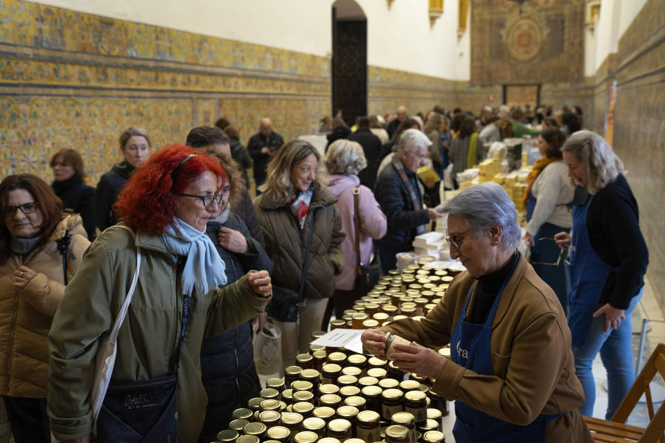 Customers buy marmalades and cakes made by cloistered nuns, at a market at the Reales Alcazares in Seville, Spain, on Tuesday, Dec. 5, 2023. Most monasteries have to be financially self-sufficient. Many in countries like Spain have to maintain not only an aging, shrinking cohort of monks and nuns, but also monumental, centuries-old buildings, said Fermín Labarga, a professor of church history at the University of Navarra in Pamplona. (AP Photo/Laura Leon)