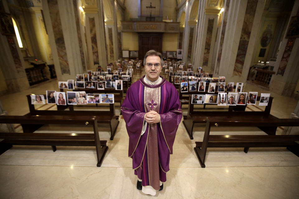 In this photo taken on March 15, 2020, Robbiano Church parson, Don Giuseppe Corbari, poses in front of selfies he was sent by parishioners as Masses for the faithful had been suspended following Italy's coronavirus emergency, in Giussano, northern Italy. Masses with the presence of faithful resumed Monday, May 18, 2020, as Italy is easing its lockdown measures. (AP Photo/Luca Bruno)