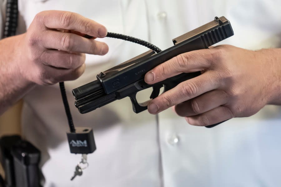 A law enforcement official demonstrates the use of a cable style gun lock on a Glock 17 pistol in Philadelphia, Wednesday, May 10, 2023. (AP Photo/Matt Rourke)