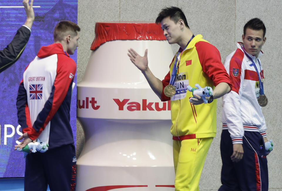 FILE - In this Tuesday, July 23, 2019 file photo, gold medalist China's Sun Yang, centre, gestures to Britain's bronze medalists Duncan Scott, left, following the medal ceremony in the men's 200m freestyle final at the World Swimming Championships in Gwangju, South Korea. Chinese swimmer Sun Yang has been banned for eight years for breaking anti-doping rules and will miss the 2020 Tokyo Olympics. (AP Photo/Mark Schiefelbein, File)