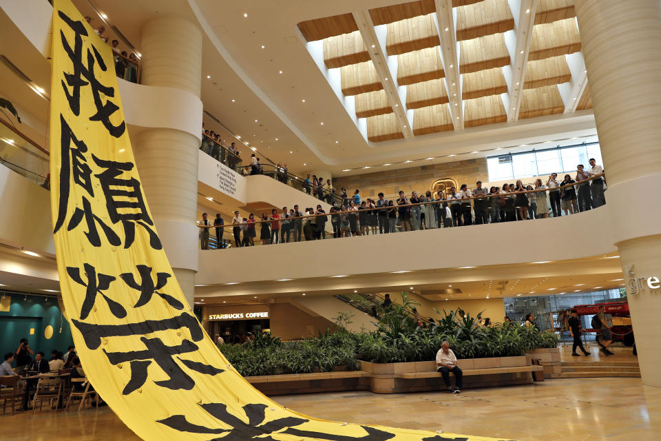 People watch protesters unfurl a banner that reads "I wish glory to Hong Kong" while playing a song titled "Glory to Hong Kong" at a Pacific Place shopping mall in Hong Kong, Wednesday, Sept. 25, 2019. Hong Kong leader Carrie Lam said Tuesday, Sept. 24 she doesn't expect a town hall meeting this week to find answers to the months-long pro-democracy protests but hopes it will be a step forward in the "long journey" to reconciliation. (AP Photo/Vincent Thian)