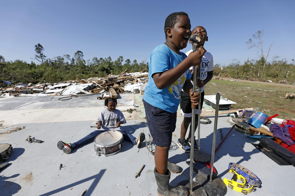 Kaden Poole, 10, foreground and his cousin Bralyn Washington, 9, sing a hymn while Ca'Loni Booth, 6, bangs away at what remains of the drum set on the slab that was James Hill Church in Prentiss, Miss., Tuesday, April 14, 2020. The church and much of its south Prentiss neighborhood was heavily damaged by a tornado Sunday, one of several that swept the state, causing a number of deaths. (AP Photo/Rogelio V. Solis)