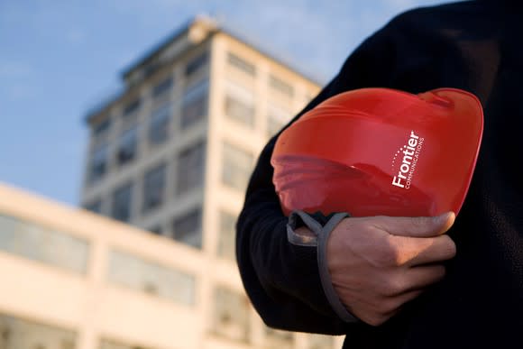 Red Frontier hat carried in the crook of someone's arm in front of a tall building.