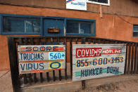 In this Sunday, Aug. 9, 2020, photo, a hand-painted sign at a post office keeps score of the COVID-19 cases and deaths in the village of Truchas, New Mexico. Nearby wilderness areas and logging roads have allowed residents to hunker down with family cookouts and outdoor recreation. (AP Photo/Cedar Attanasio)