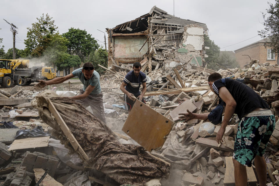 Local residents search for documents of their injured friend in the debris of a destroyed apartment house after Russian shelling in a residential area in Chuhuiv, Kharkiv region, Ukraine, Saturday, July 16, 2022. (AP Photo/Evgeniy Maloletka)