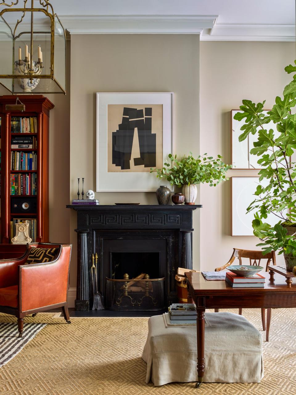 A custom scagliola mantel designed by Schafer and fabricated by plaster artisan Ahmad Suleiman dominates a light-filled corner of the living room. The artwork is by Jack Sonenberg. An antique dining table purchased in Bath, England, serves as a desk for post-office late-night work; it’s paired with a 19th-century leather and wood library chair.