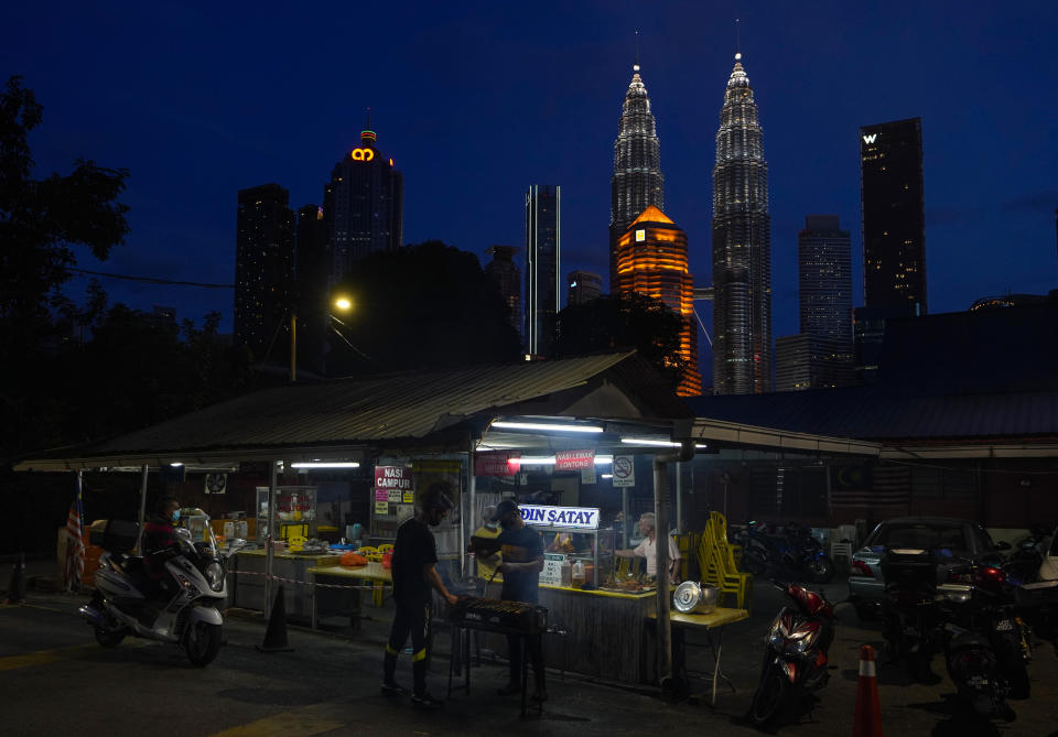 A local food vendor prepares food with the Twin Towers in downtown Kuala Lumpur in the background background, Malaysia, Monday, Jan. 11, 2021. Prime Minister Muhyiddin Yassin says Malaysia's health care system is at a breaking point as he announced new movement curbs, including near-lockdown in Kuala Lumpur and several high-risk states to rein in a spike in coronavirus cases.(AP Photo/Vincent Thian)