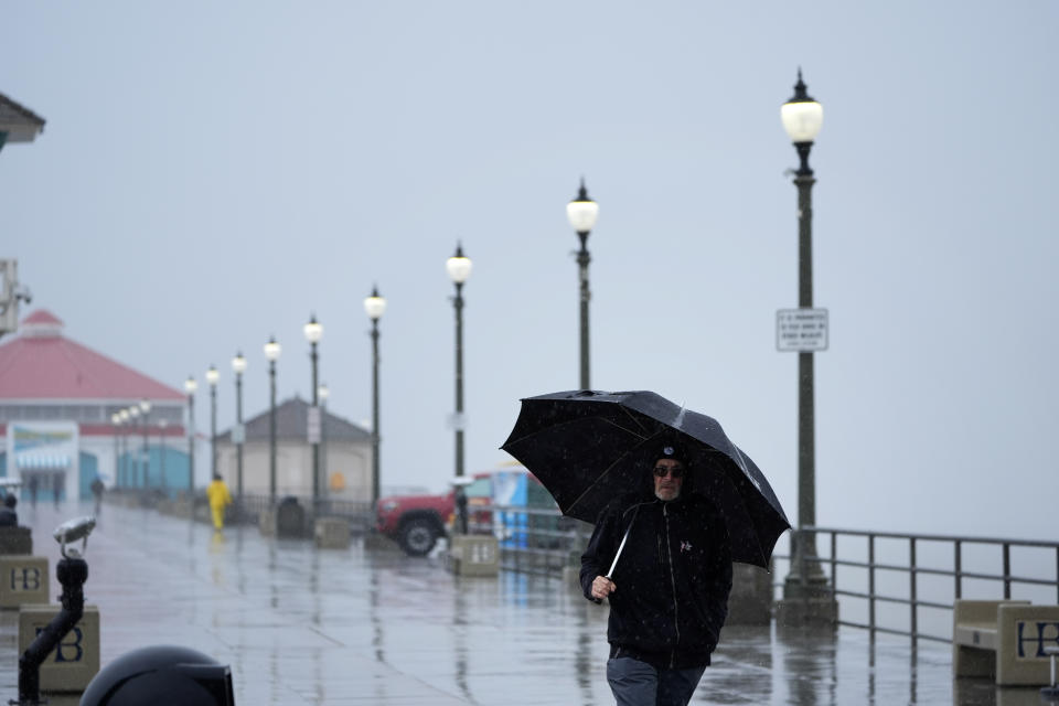 A man shields himself from the rain as he walks along the Huntington Beach Pier on Tuesday, Feb. 6, 2024, in Huntington Beach, Calif. (AP Photo/Marcio Jose Sanchez)
