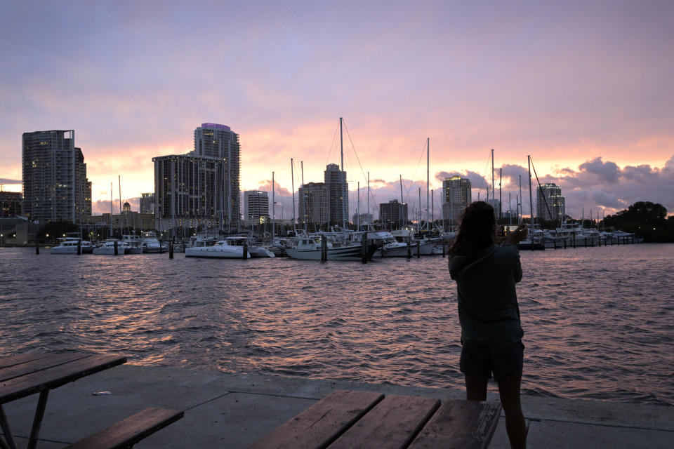 Kristi Burghdurf makes a photo of the sunset with her phone as an outer band of Hurricane Ian passes the waterfront of Tampa Bay, Tuesday, Sept. 27, 2022, in St. Petersburg, Fla. (AP Photo/Phelan M. Ebenhack)