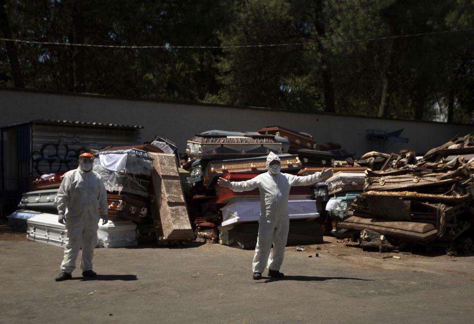 An employee of Xochimilco's crematorium directs a hearse into the unloading area, as him and another employee wait for the corpse of a person suspected to have died of the new coronavirus, in Mexico City, Monday, May 4, 2020. The men are standing next to pile of discarded coffins that contained people who died of COVID-19 disease, and are waiting to be destroyed at the site. (AP Photo/Fernando Llano)