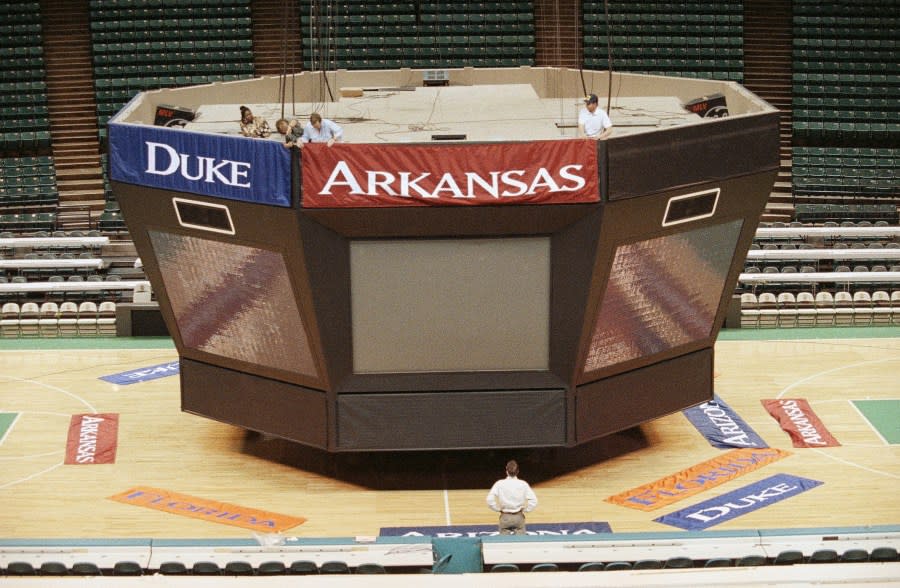 Workers at the Charlotte Coliseum hang banners for the Final Four teams on the scoreboard, Tuesday, March 29, 1994, Charlotte, N.C. The banners of the four teams, Duke, Arkansas, Florida, and Arizona, will cover panels that normally carry advertising. (AP Photo/Chuck Burton)