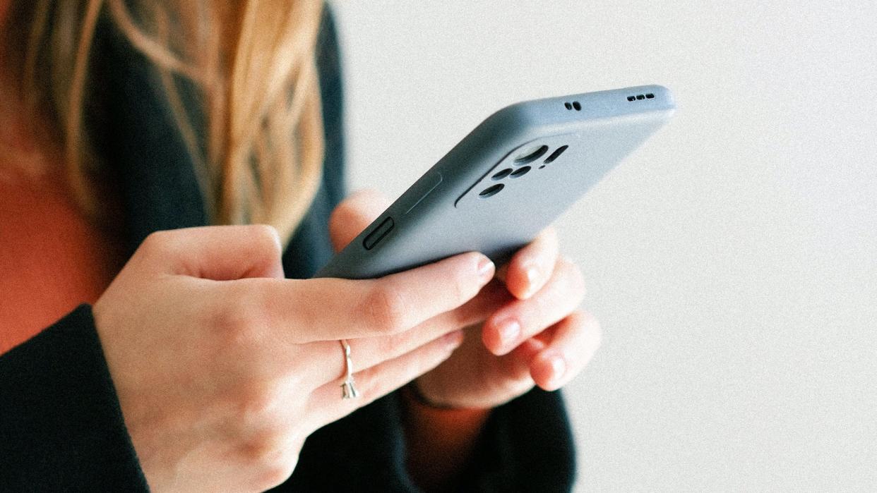 Person in a red sweater and a black coat holds a mobile phone on their hands and looks at the screen.