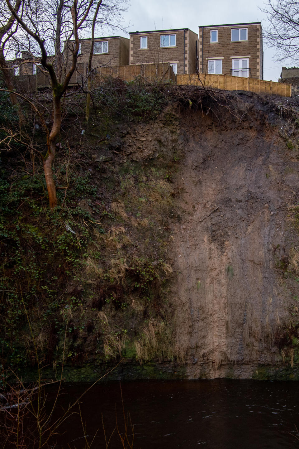 The back gardens of residential properties in Slaithwaite sit precariously near to the edge of a landslide on the banks of the River Colne near Huddersfield after flooding.