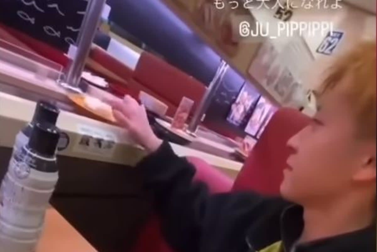 A boy licks his fingers and then fingers sushi that willl be eaten by another customer at a Japanese restaurant (@takigare3/Twitter)