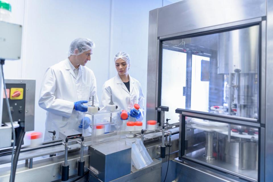 Colleagues inspect bottles of pills in a factory