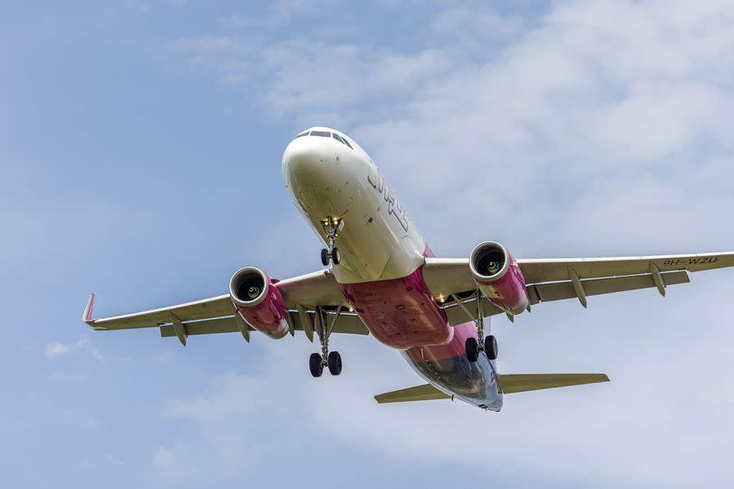A Wizz Air plane descending through blue skies to land