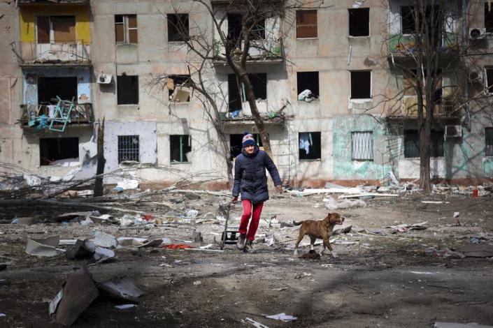 Un hombre camina con su perro cerca de un edificio de apartamentos da&#xf1;ado por los bombardeos de los combates en las afueras de Mariupol.