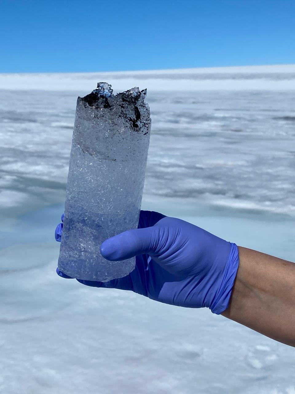 gloved hand holds up ice core with one end stained black