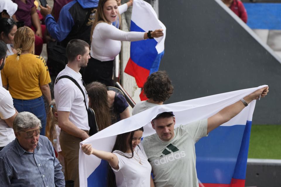 Spectators drape themselves with a Russian national flag during the Alba Games' opening ceremony, inside the baseball stadium in La Guaira, Venezuela, Friday, April 21, 2023. (AP Photo/Ariana Cubillos)