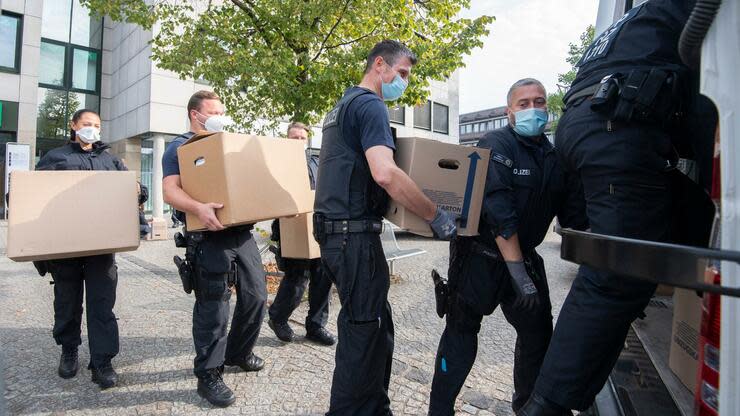 Bundespolizisten tragen bei einer Razzia Kartons mit beschlagnahmten Unterlagen aus einem Bürogebäude. Foto: dpa