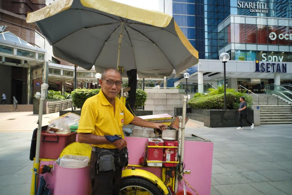 An elderly ice cream seller poses next to his ice cream cart along Orchard Road.