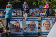 A volunteer hands out "how to vote cards" as voters walk past billboards of Independent candidate Zali Steggall outside a polling booth in her electorate of Warringah in Sydney, Australia on May 17, 2022. Australia's government, considered a laggard on combating climate change, faces a new threat in the form of highly-organized and well-funded independent election candidates who demand deeper cuts on greenhouse gas emissions. (AP Photo/Mark Baker)