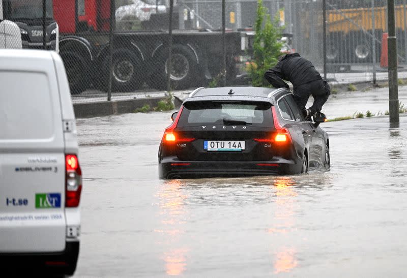 Man climbs out of a car that tried to get through a flooded roundabout in Arlov