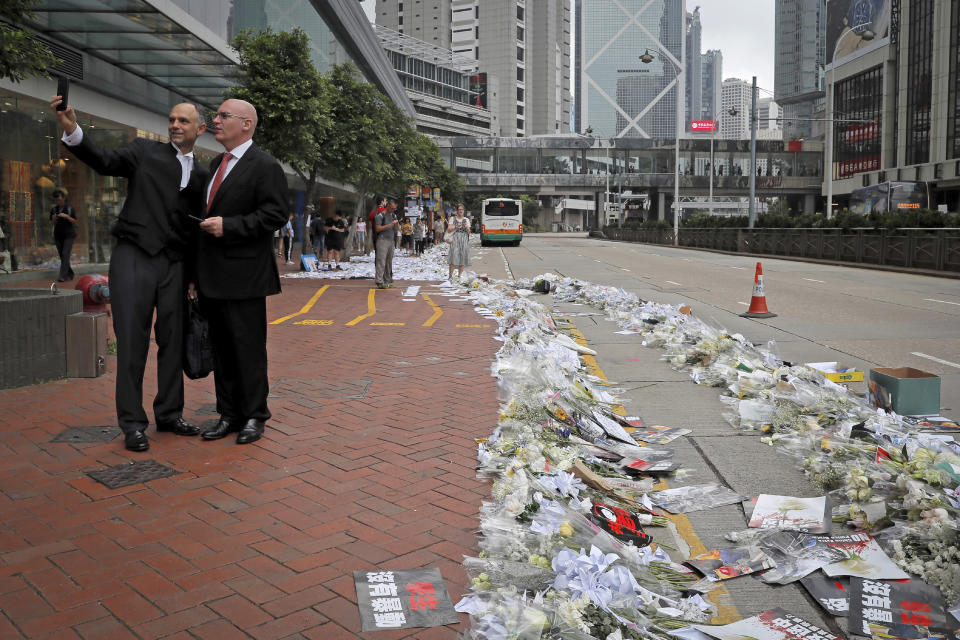 In this Monday, June 17, 2019, photo, foreigners take a selfie near posters and flowers placed on a street after tens of thousands of protesters staged a massive protest against the unpopular extradition bill in Hong Kong. All but a handful of protesters in Hong Kong have gone home, but the crisis that brought nearly 2 million into the streets to oppose the extradition bill is far from over. (AP Photo/Kin Cheung)