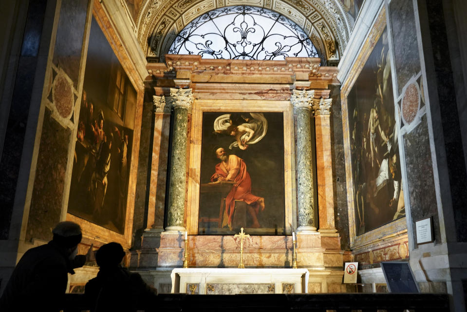 Visitors admire a cycle of paintings by 16th century artist Michelangelo Merisi, known as Caravaggio, on the life of St.Matthew, inside the Contarelli chapel of San Luigi dei Francesi Church, in Rome, Friday, Dec. 11, 2020. Like elsewhere in Europe, museums and art galleries in Italy were closed this fall to contain the spread of COVID-19, meaning art lovers must rely on virtual tours to catch a glimpse of the treasures held by famous institutions such as the Uffizi in Florence and the Vatican Museums in Rome. However, some exquisite gems of Italy's cultural heritage remain on display in real life inside the country's churches, some of which have collections of renaissance art and iconography that would be the envy of any museum. (AP Photo/Andrew Medichini)