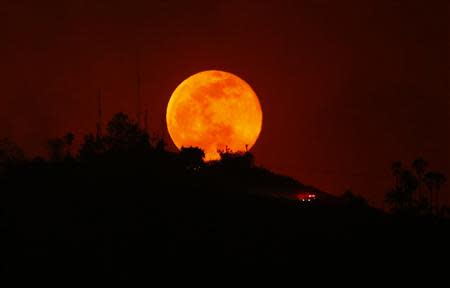 An emergency vehicle makes is way past a rising moon as it travels along a burned-out hillside near San Marcos, California May 14, 2014. REUTERS/Mike Blake