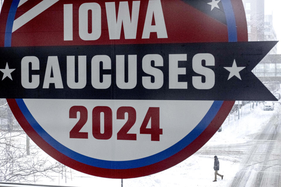 A man walks across the street below a sign for the Iowa Caucuses in downtown Des Moines, Iowa, Saturday, Jan. 13, 2024. (AP Photo/Andrew Harnik)