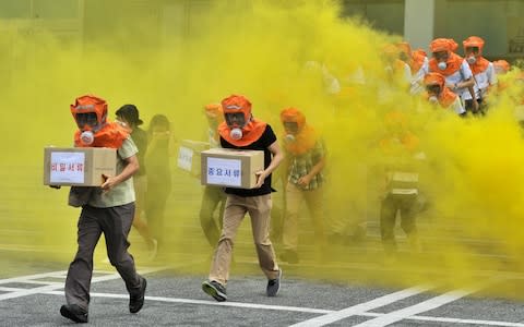 South Koreans wearing gas masks run out of a building during a civil defence drill in Seoul  - Credit: AFP