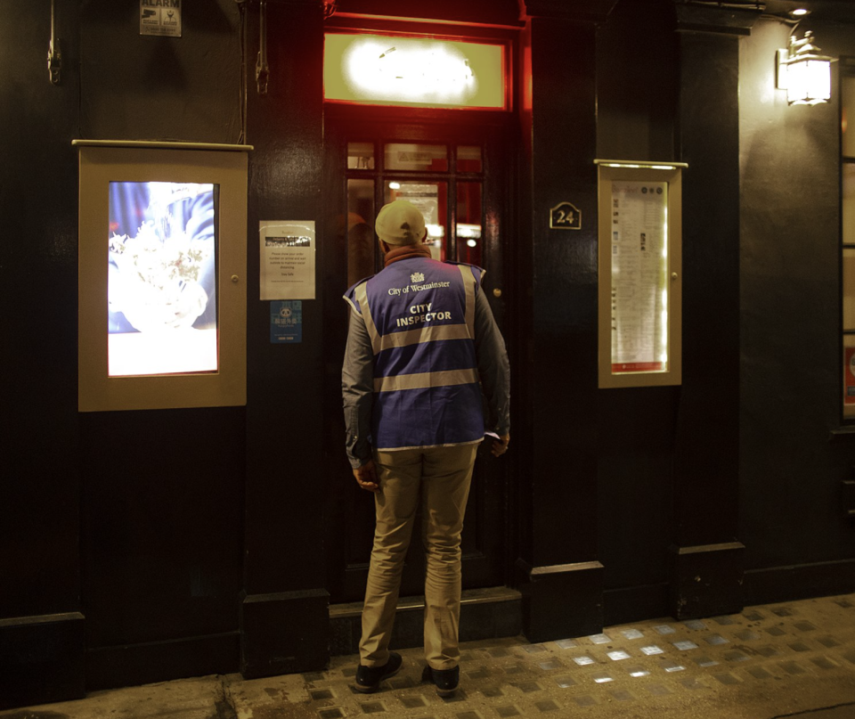 A city inspector peeking through the door of an establishment in London.