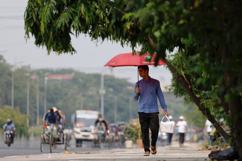 A man walks along a road with an umbrella to cover himself from the sun during a countrywide heatwave in Dhaka