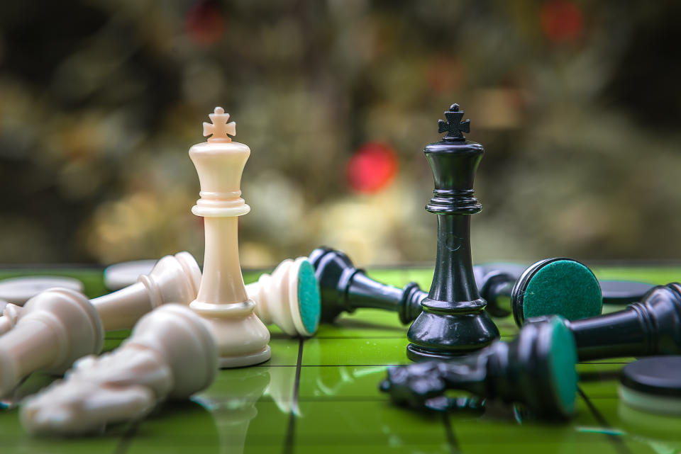 Two king chess pieces surrounded by other chess pieces that were knocked over