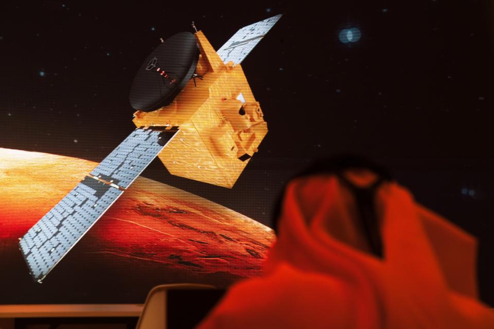 An Emirati television journalist works on a script as a graphic showing the Emirates' Hope space probe to Mars flashes past him on a screen at the Mohammed bin Rashid Space Center in Dubai, United Arab Emirates, Sunday, July 19, 2020. A Japanese H-IIA rocket carrying a United Arab Emirates Mars spacecraft has been placed on the launch pad for Monday's scheduled liftoff for the Arab world's first interplanetary mission, officials said Sunday. (AP Photo/Jon Gambrell)