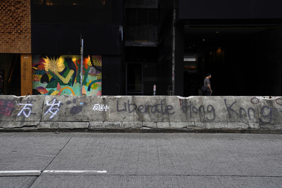 In this Sept. 16, 2019, photo, a man walks by the road block with anti-government graffiti. The most common graffiti is "Liberate Hong Kong, Revolution of Our Times." Other messages include the popular chant "Five Demands and Not One Less," expressing demands for greater democracy. As Hong Kong enters its fourth month of steady protests, the city is embracing for another violent weekend prior to the upcoming 70th National Day on Oct. 1. (AP Photo/ Vincent Yu)