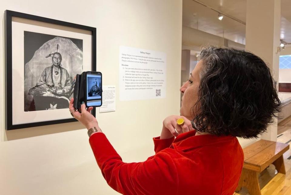 Alexandra Nicholis Coon, executive director of the Massillon Museum, demonstrates how to learn more about a new exhibit through the use of a cellphone. The exhibit is titled, "Un-settling: A Story of Land Removal and Resistance."