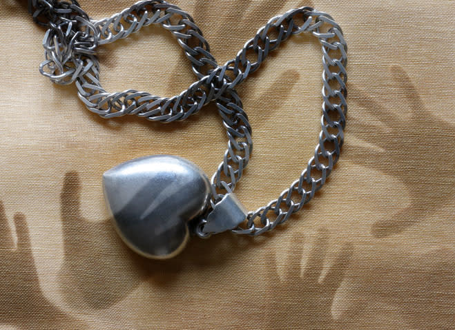 Silver heart pendant on a chain, lying on a textured fabric surface