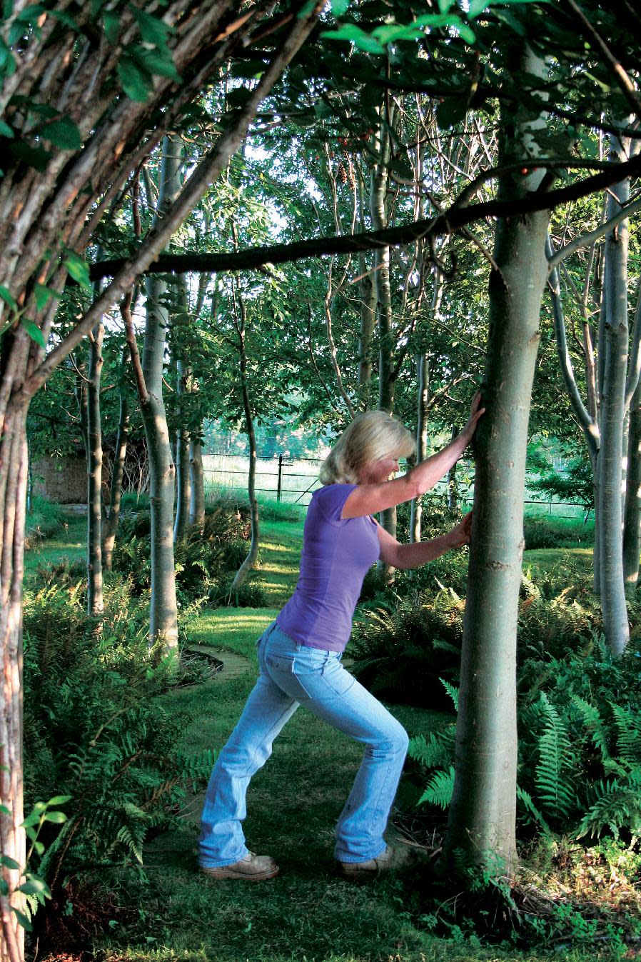 This undated publicity photo released by courtesy Timber Press, shows Bunny Guinness using a tree to stretch for exercise from the book, “Garden Your Way To Health and Fitness,” by Bunny Guinness and Jacqueline Knox (Design, Bunny Guinness). Gardening can be a formidable workout and calorie burner, especially when adding calisthenics to the mix, along with stretching to avoid cramping and joint pain. (AP Photo/ Courtesy Timber Press)