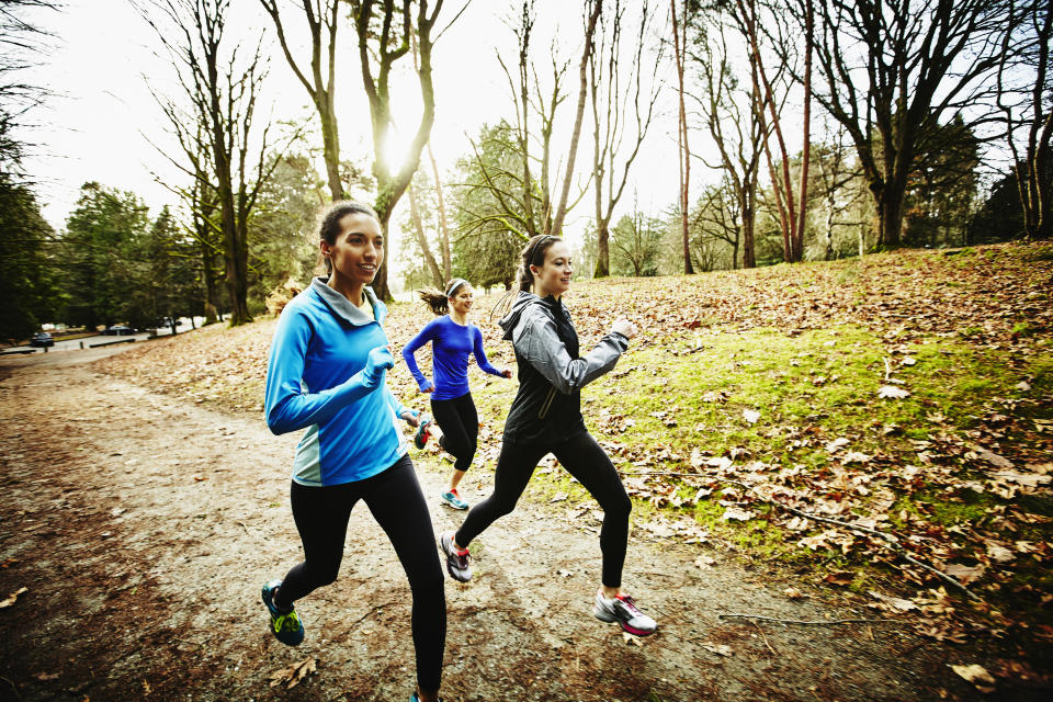 Smiling group of female friends running trails together in park on winter morning 