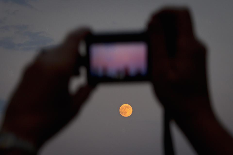 A woman takes a photo of the moon one day ahead of the Supermoon phenomenon from a bridge over 42nd St. in the Manhattan borough of New York