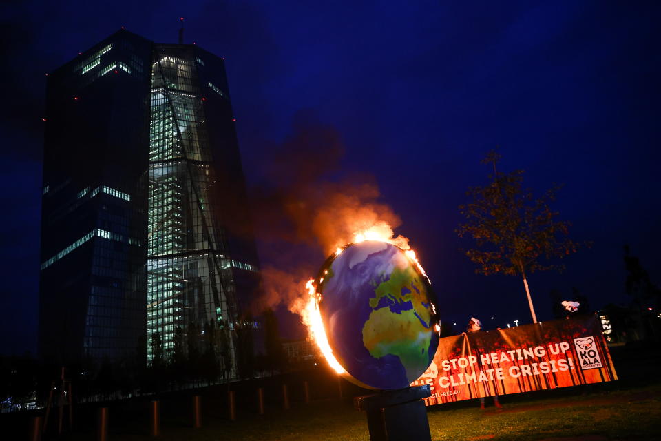 Protesters hold a banner as a paper made globe is seen burning during a demonstration against the fossil fuel industry, in front of the headquarters of the European Central Bank (ECB), in Frankfurt, Germany, October 21, 2020. REUTERS/Kai Pfaffenbach