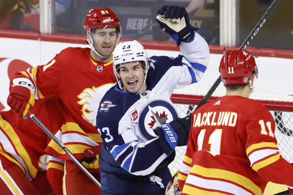 Calgary Flames' Kevin Rooney and teammate Mikael Backlund look on as Winnipeg Jets' Sean Monahan celebrates a goal during the first period of an NHL hockey game in Calgary, Alberta, Monday, Feb. 19, 2024. (Larry MacDougal/The Canadian Press via AP)