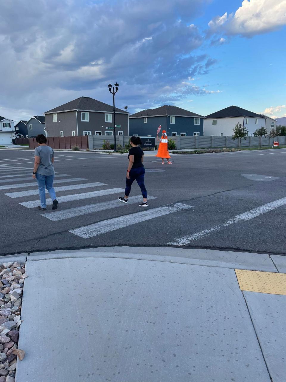 Whitney Durfee, in her traffic cone costume, helps pedestrians cross a crosswalk.