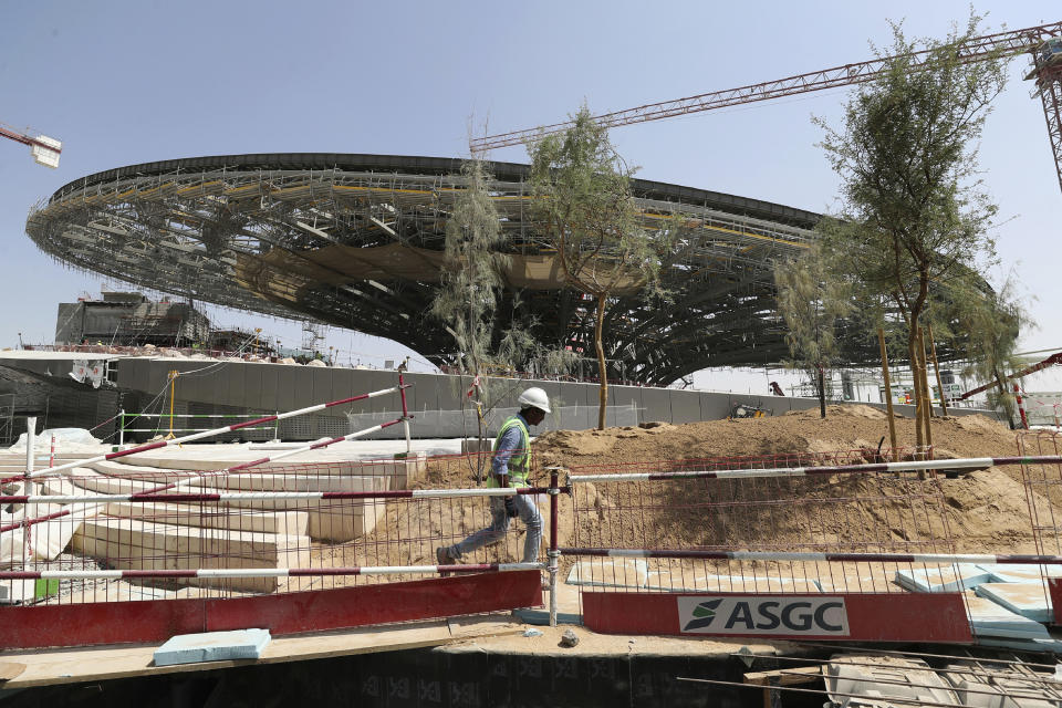 In this Oct. 8, 2019, photo, a worker passes in front of the Sustainability Pavilion at the under construction site of the Expo 2020 in Dubai, United Arab Emirates. It rises out of what were once rolling sand dunes stretching toward the horizon, a feverish construction site by tempo and temperature that has tens of thousands of workers building what looks like a new city in the desert of Dubai. (AP Photo/Kamran Jebreili)