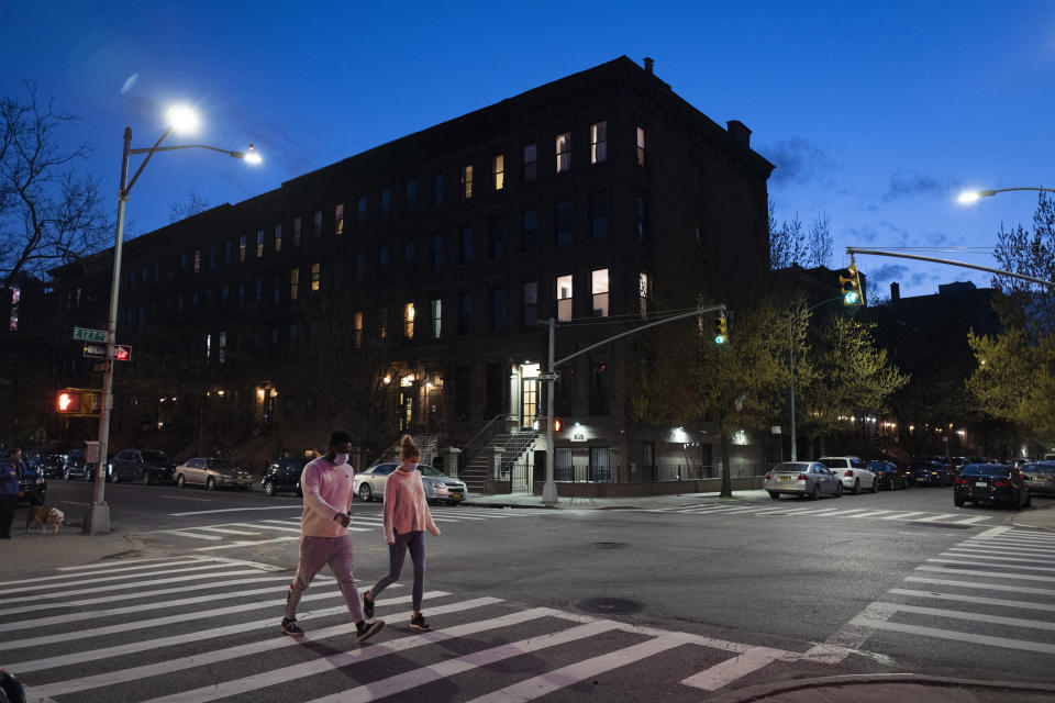People wearing masks cross the street at Langston Hughes Place in Harlem, Wednesday night, April 15, 2020 during the coronavirus pandemic in New York. Known as "The City That Never Sleeps," New York's streets are particularly empty during the pandemic. (AP Photo/Mark Lennihan)